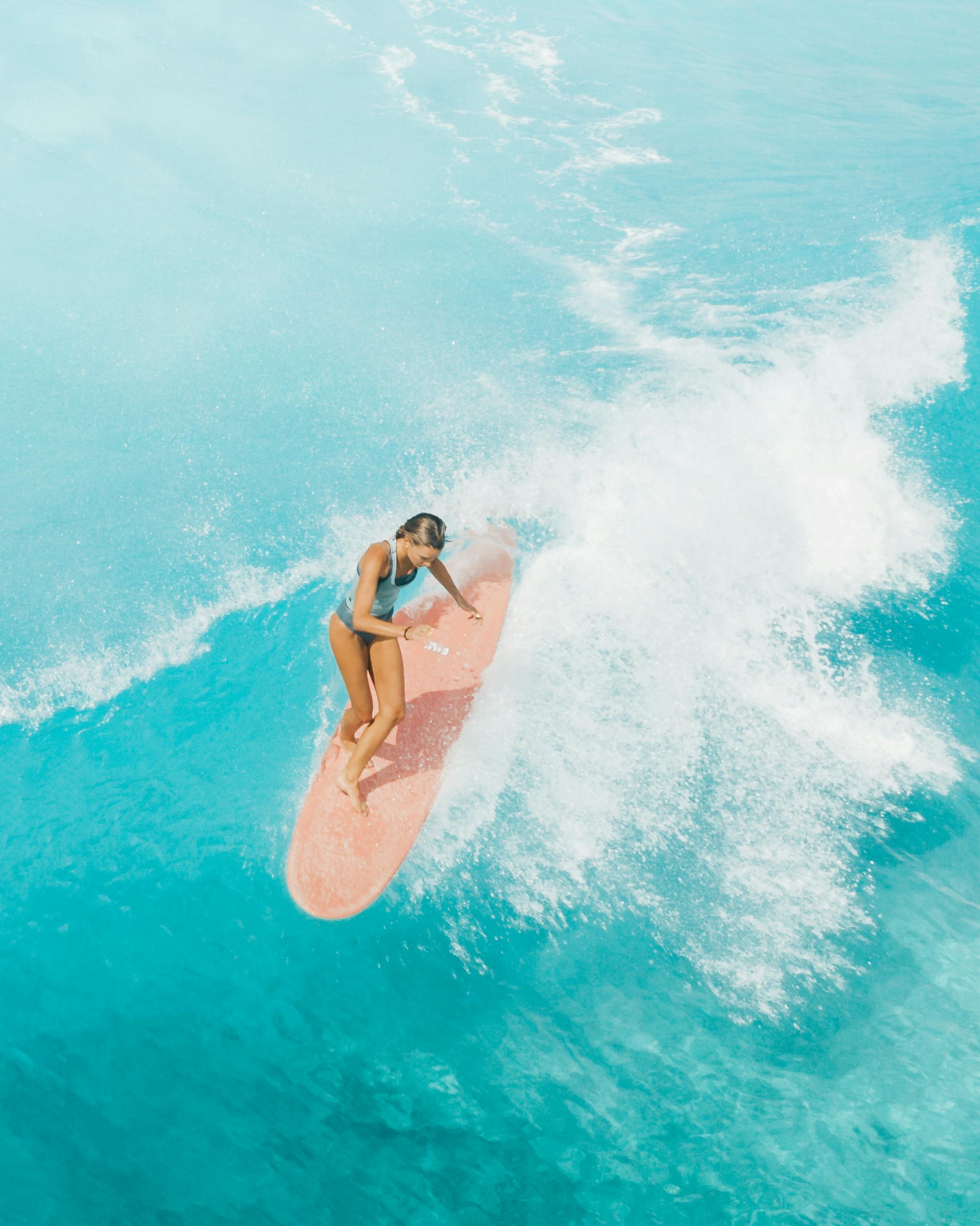 Aerial view of a female surfer skillfully riding waves on a vibrant turquoise ocean.